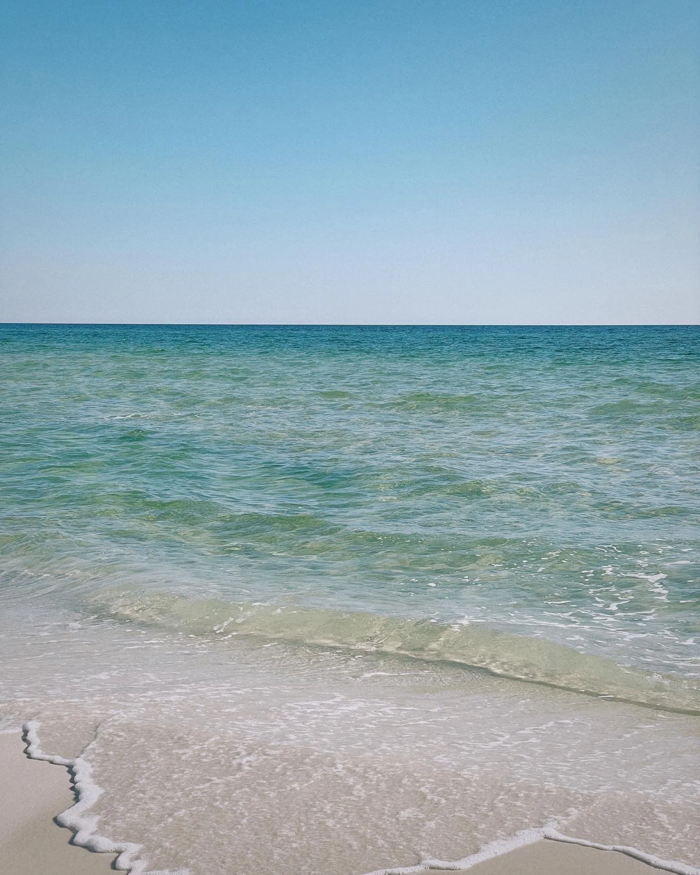 Calm ocean waves gently rolling onto a sandy beach under a clear blue sky.