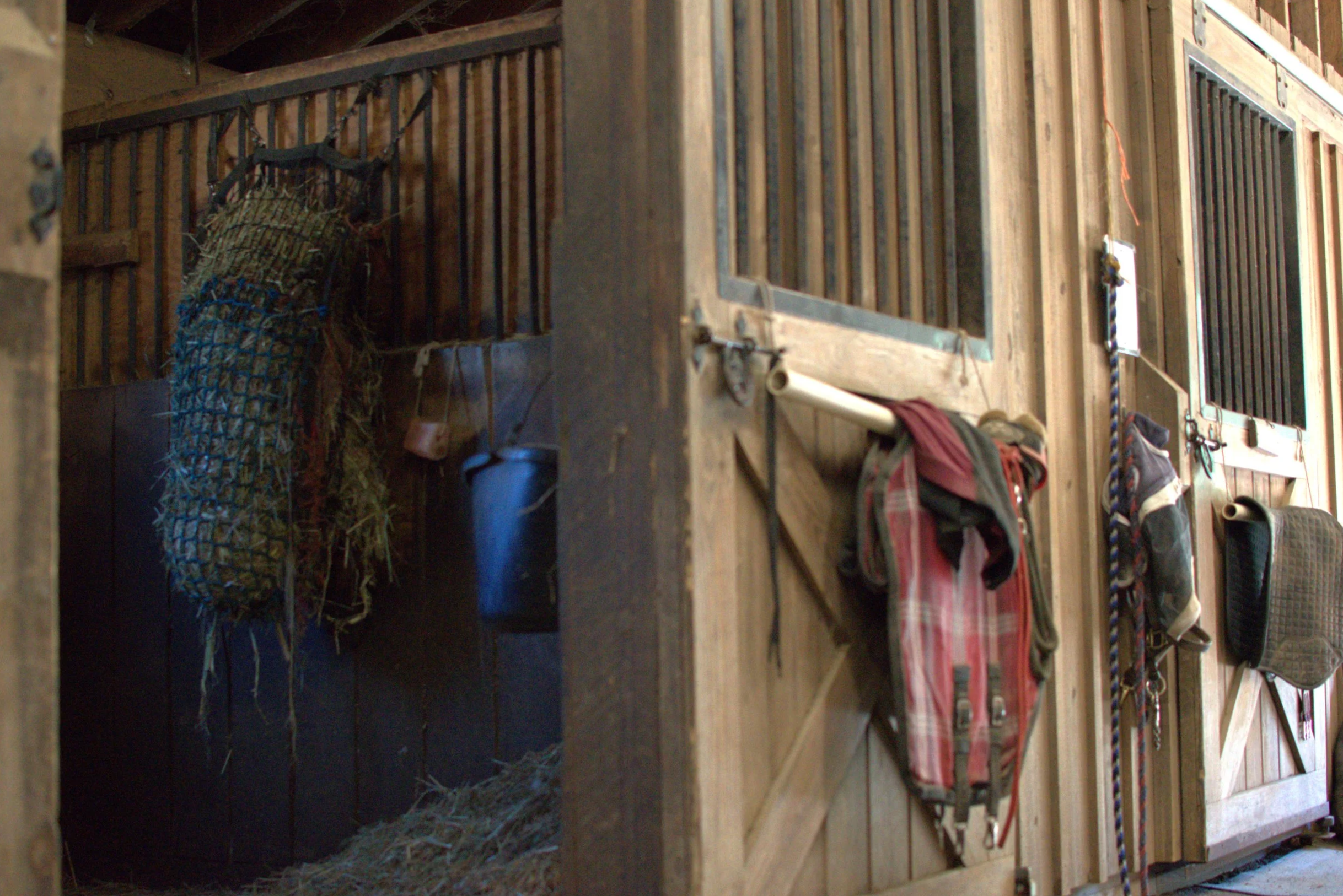 Interior of a wooden barn or shed with a hay bale, tools, and various hanging objects.