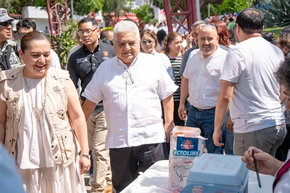 Group of people gathered outdoors, engaged in conversation around a table with medical supplies, including a box labeled 'Ectoline,' on a sunny day.