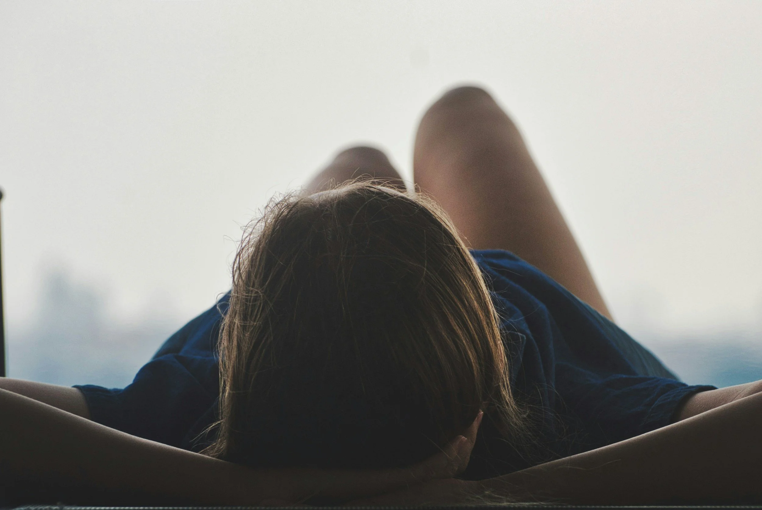 A person lying on their stomach with arms extended forward, facing downward, with their head resting on their arms and hair covering their face.