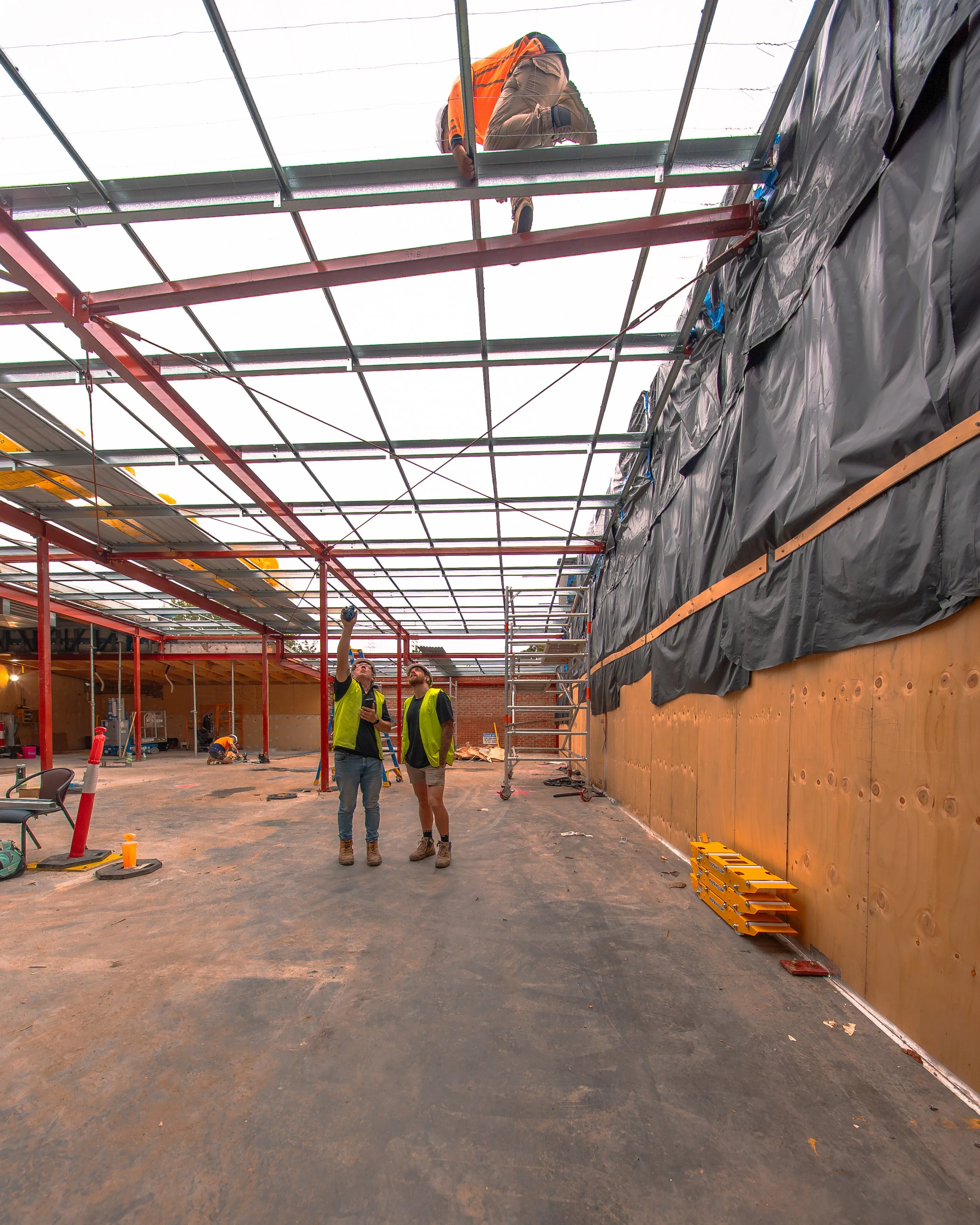 Construction workers inside a building under construction, with a partially finished ceiling, insulation, and tools on the ground.