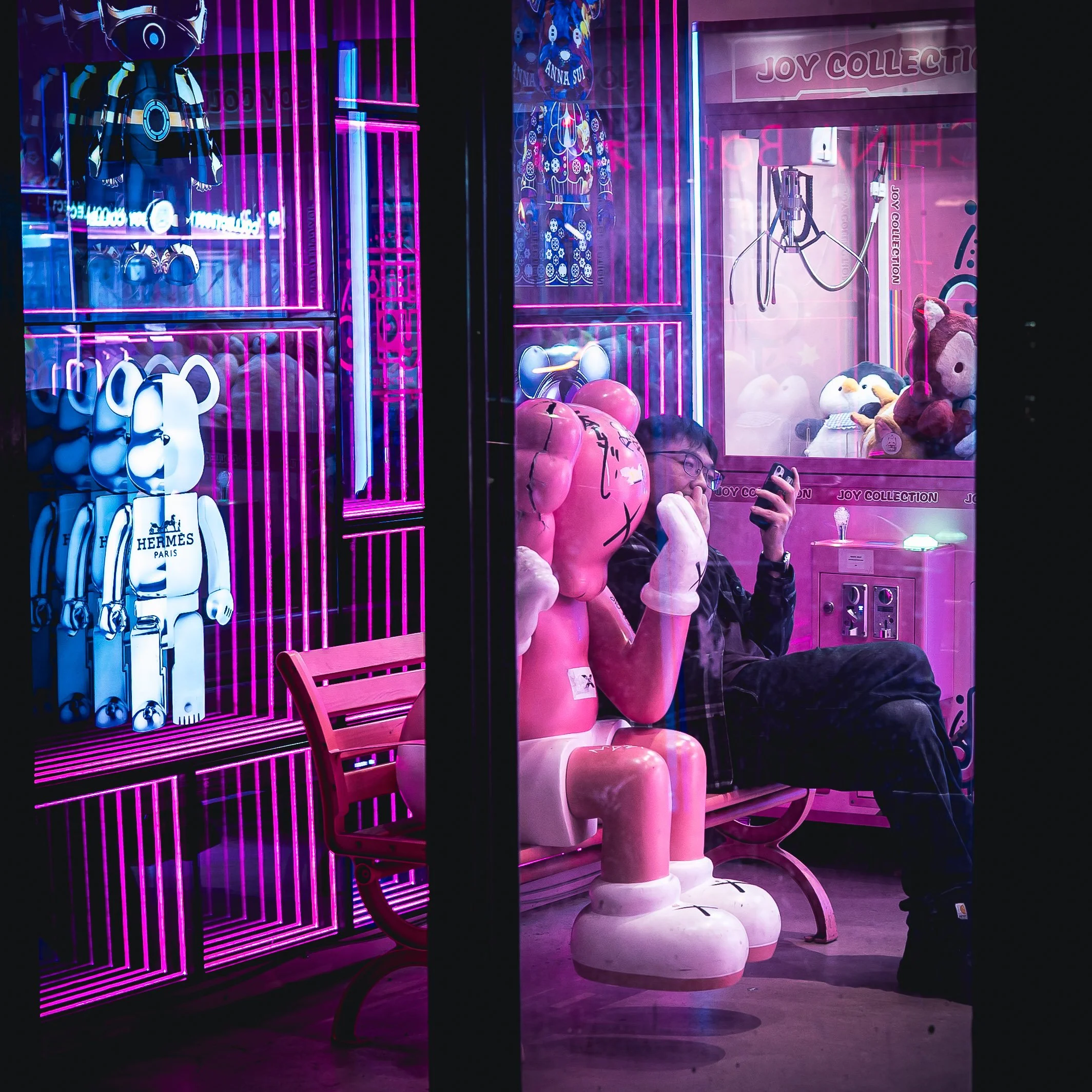 A neon-lit arcade with plush toys and arcade machines, including a robot-themed stuffed toy and pink pig-shaped plush toy, reflected in glass.