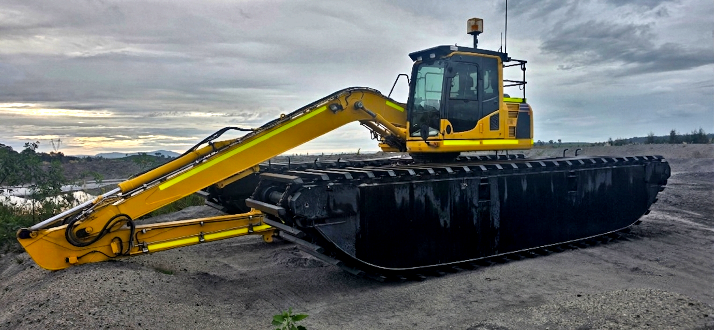 A large yellow excavator with black tracks on a construction site with an overcast sky.