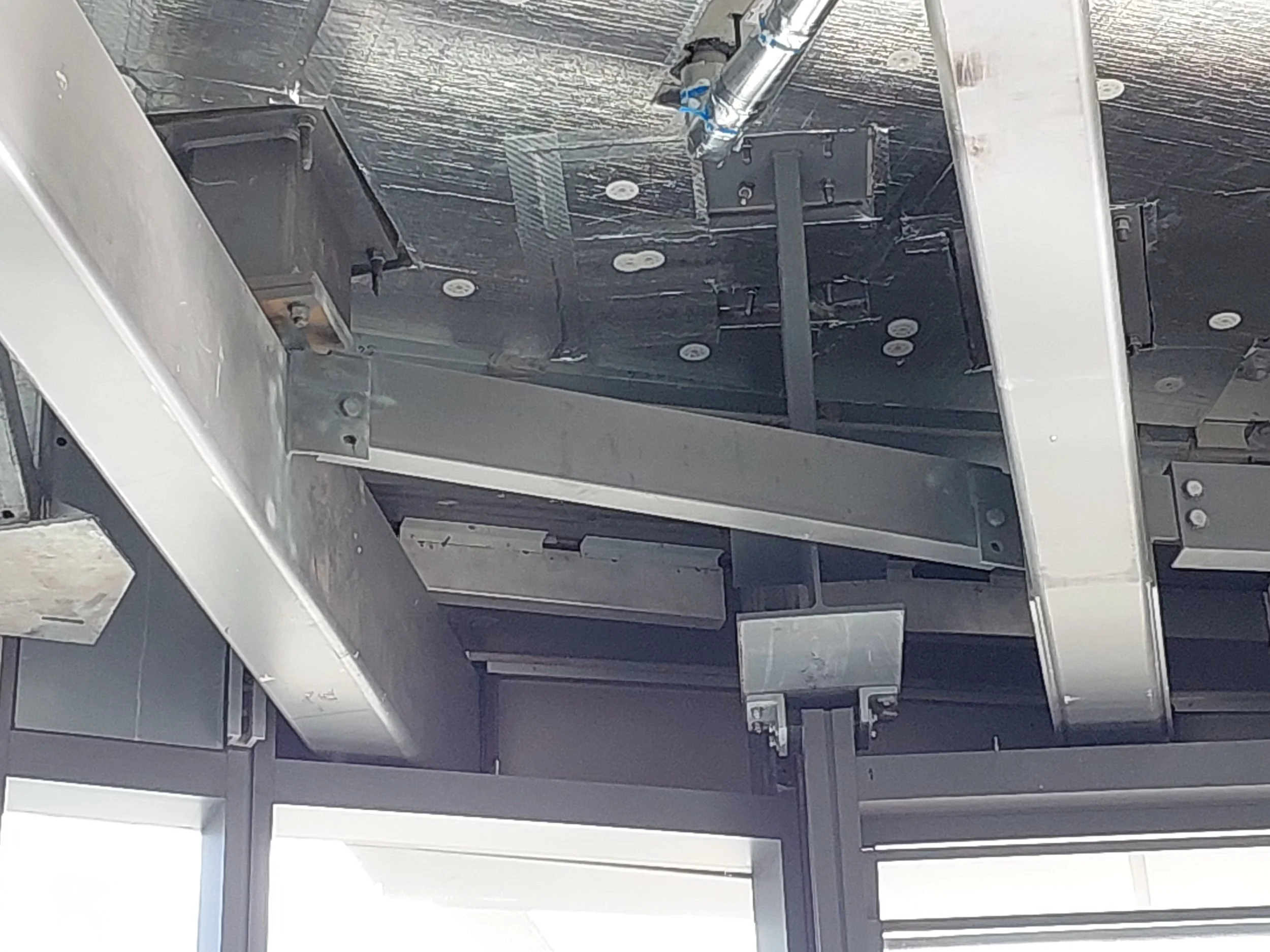 Close-up of an industrial or mechanical structure with metal beams, pipes, and black panels, some attached with bolts, in a metallic environment.