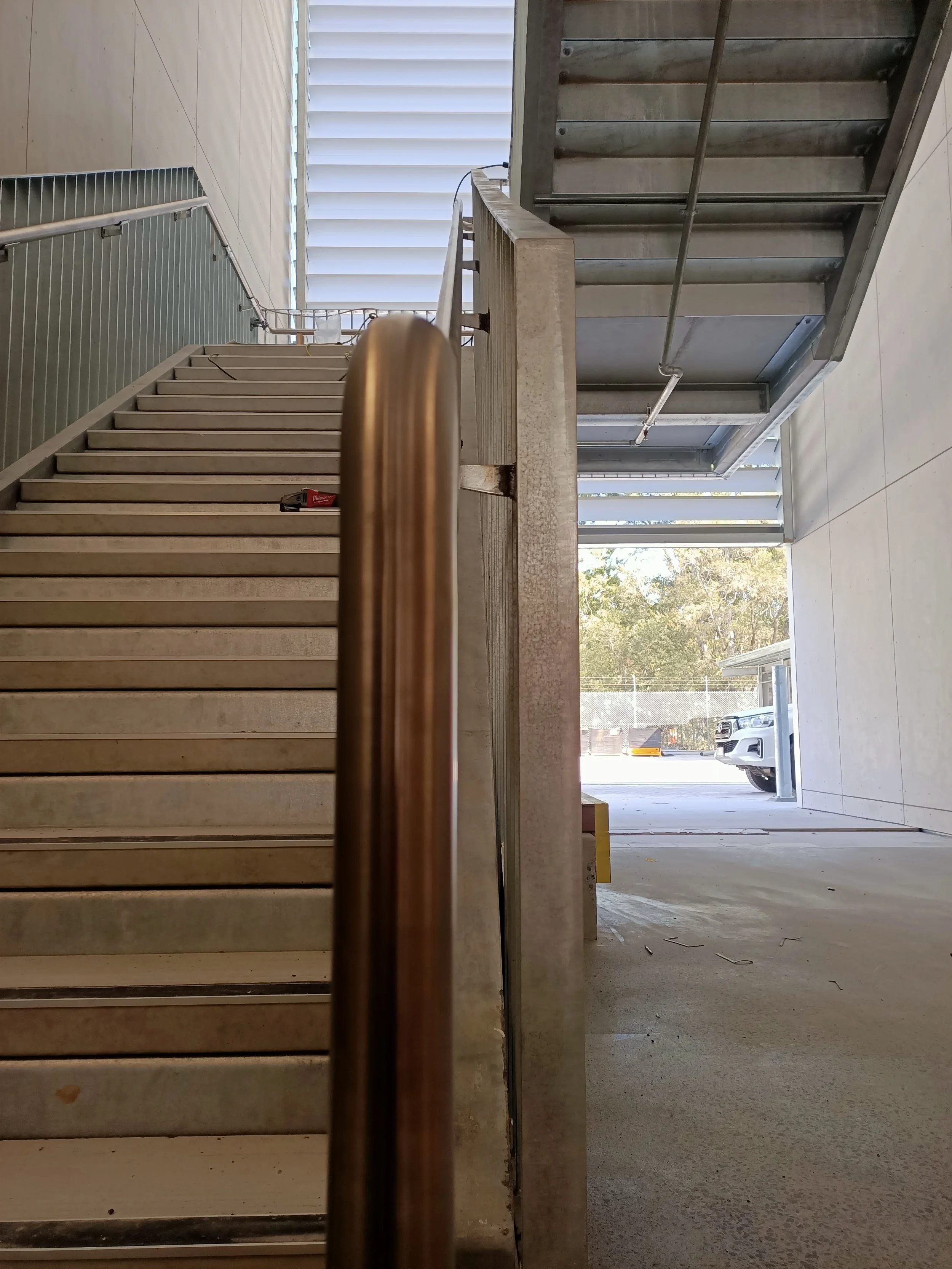 View of a staircase and air conditioning units outside a building with a parking lot and trees in the background.