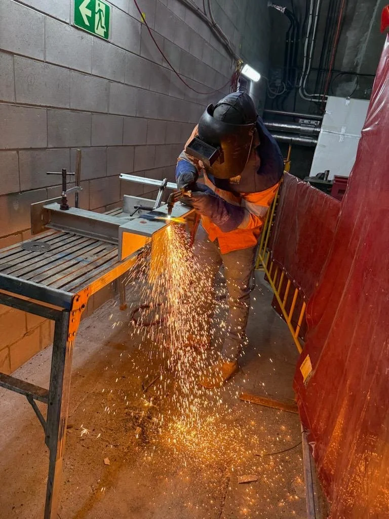 Worker in safety gear welding metal with sparks flying in an industrial workshop.