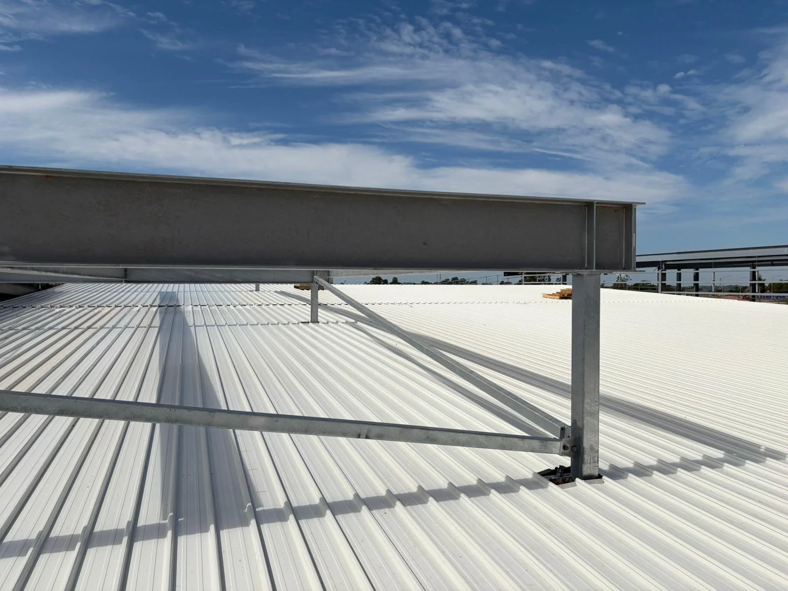 View of a metal rooftop with a large metal beam structure on top, under a partly cloudy sky.
