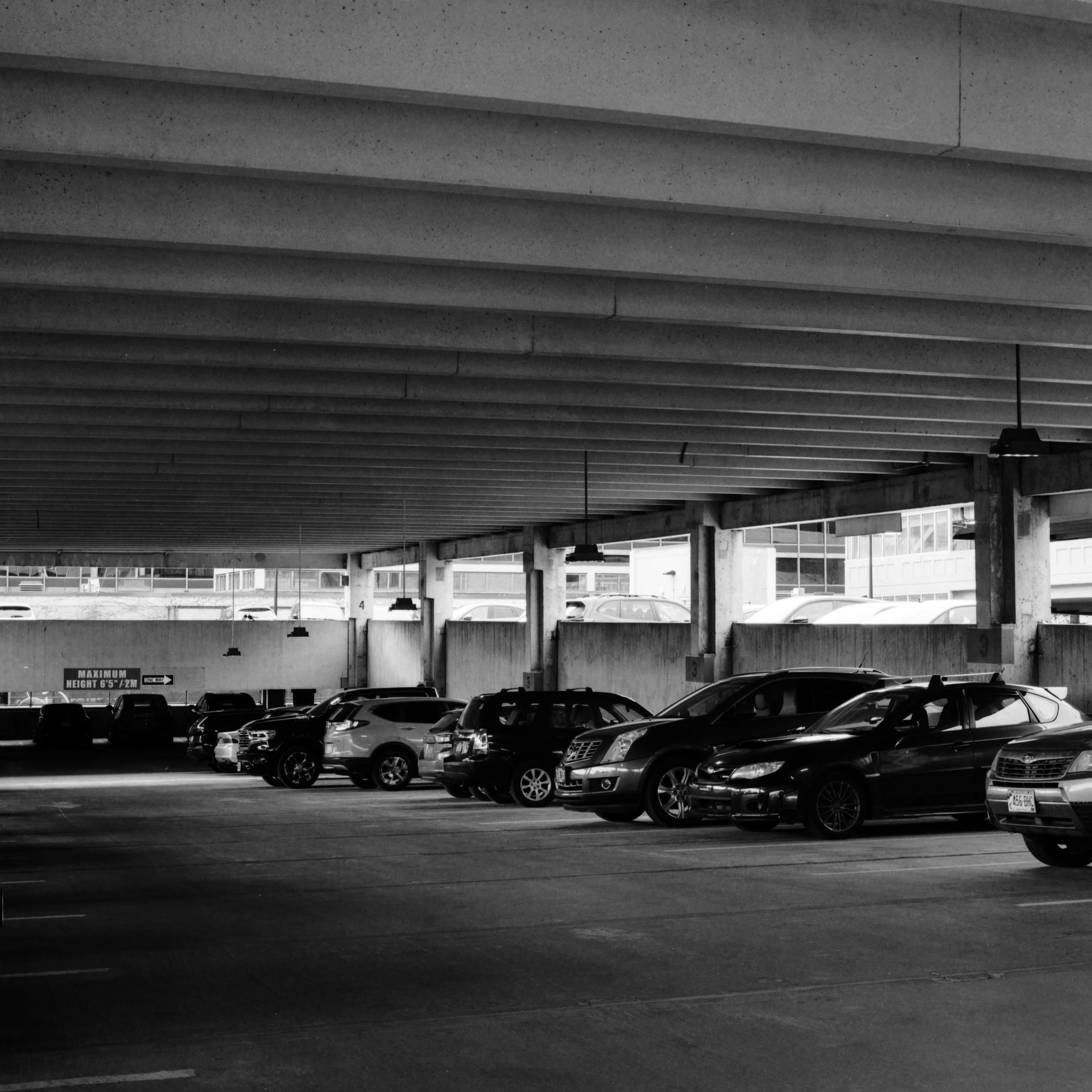 Black and white photograph of a parking garage with cars parked on the lower level and a concrete ceiling overhead.