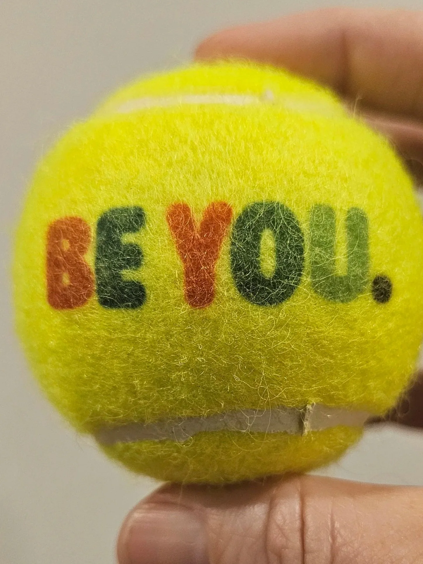 Close-up of a yellow tennis ball with the words "be you" to encourage you to put your personality on a tennis ball