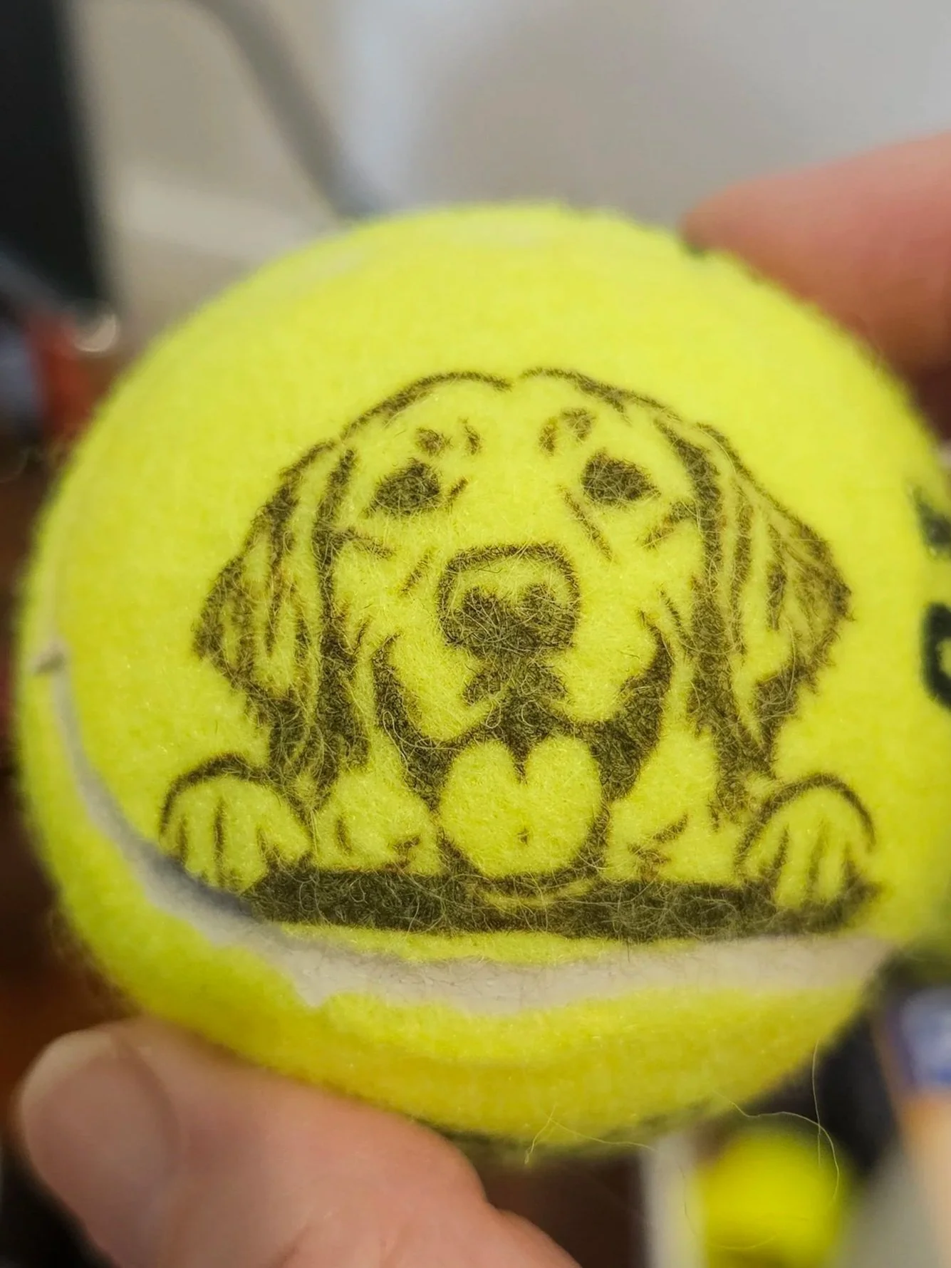 Close-up of a yellow tennis ball with a detailed image of a dog printed on it.