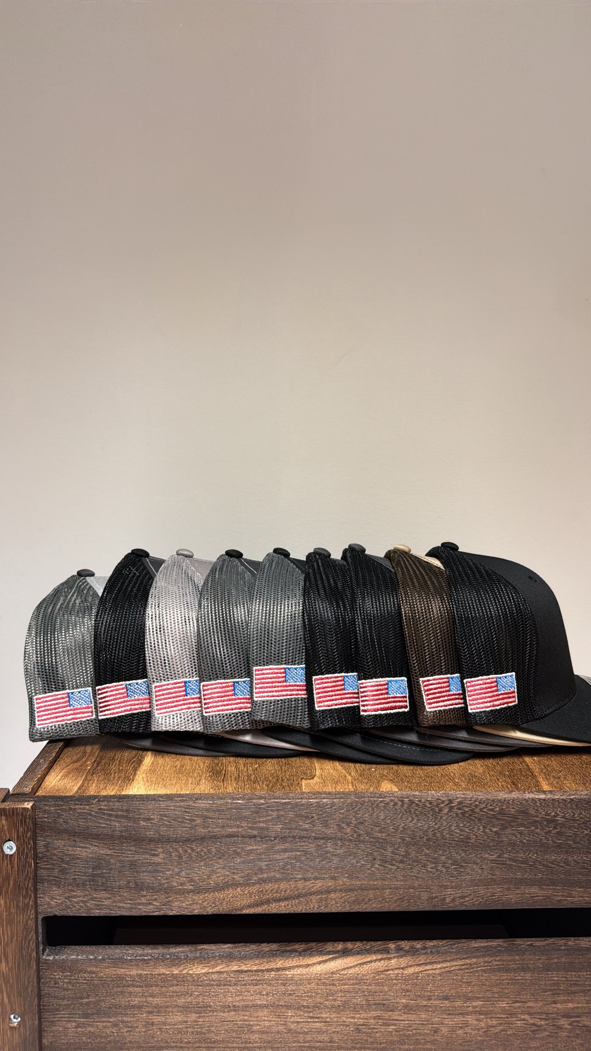 Several mesh baseball caps with American flag patches on the front, arranged in a row on a wooden table against a plain wall.
