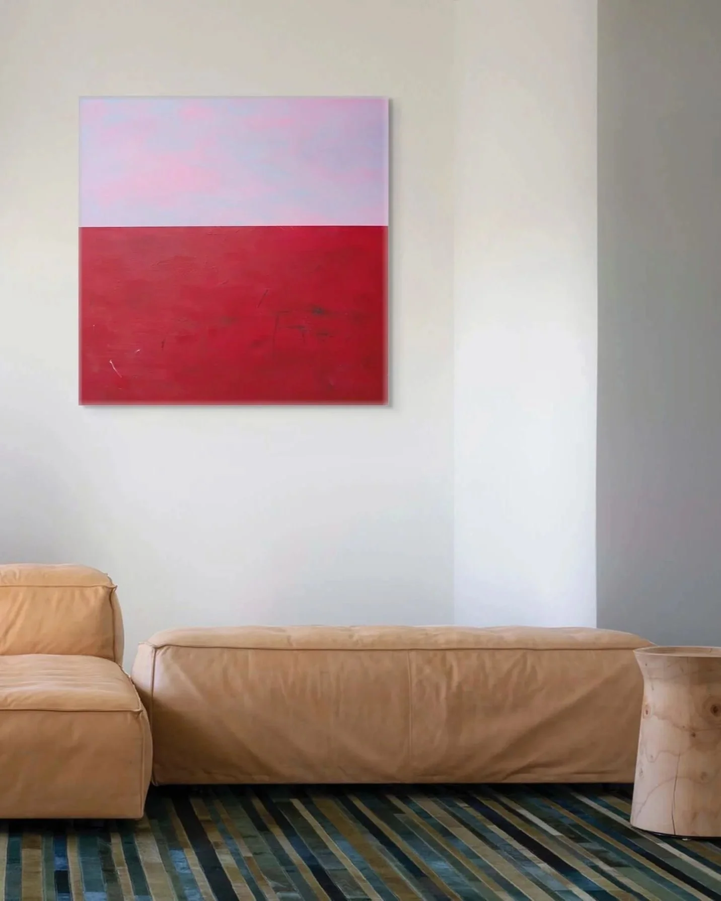 A living room with a beige couch, two beige armchairs, a colorful striped rug, an abstract painting with pink and red sections on a white wall.