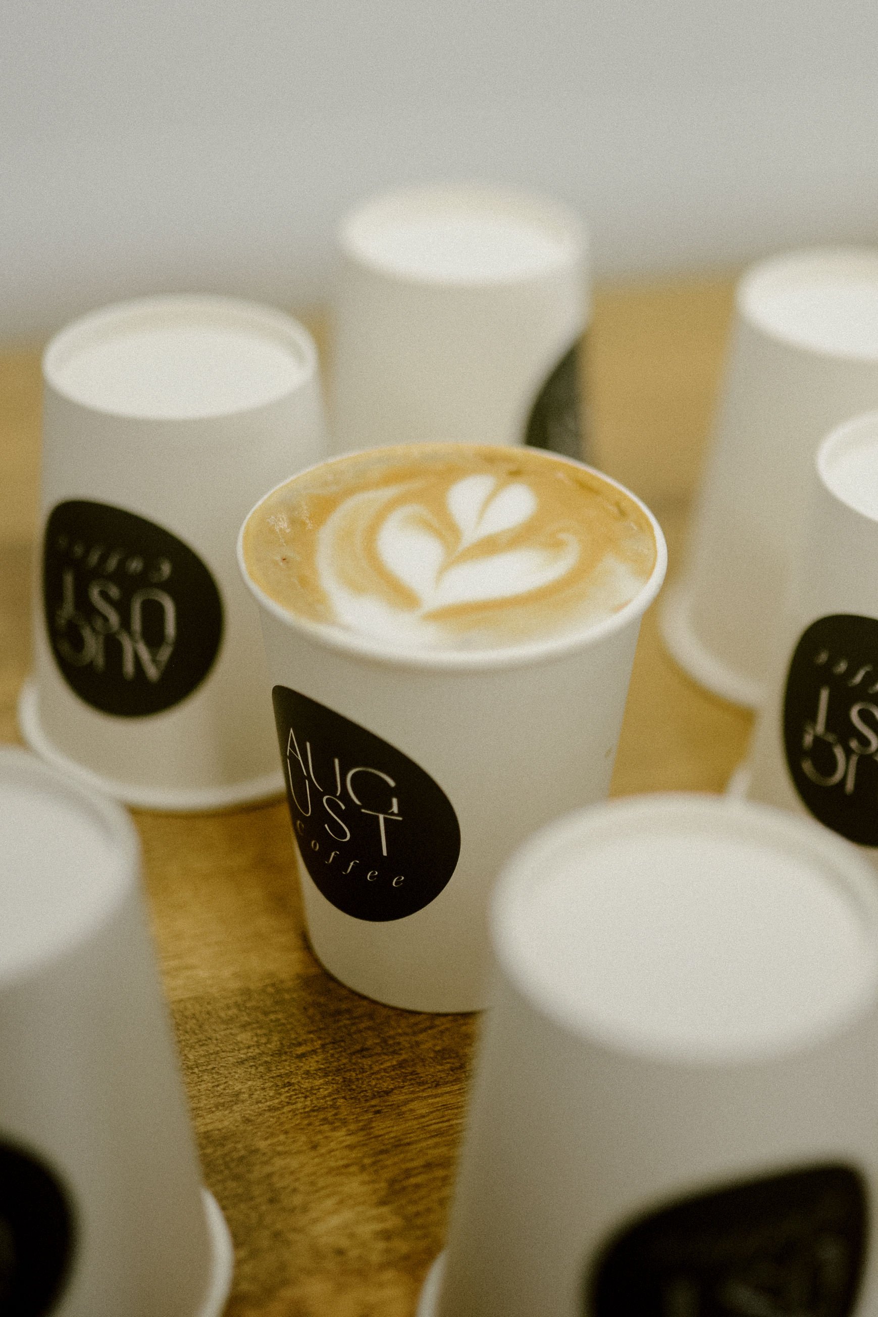 Several disposable cups of coffee with latte art on a wooden surface.
