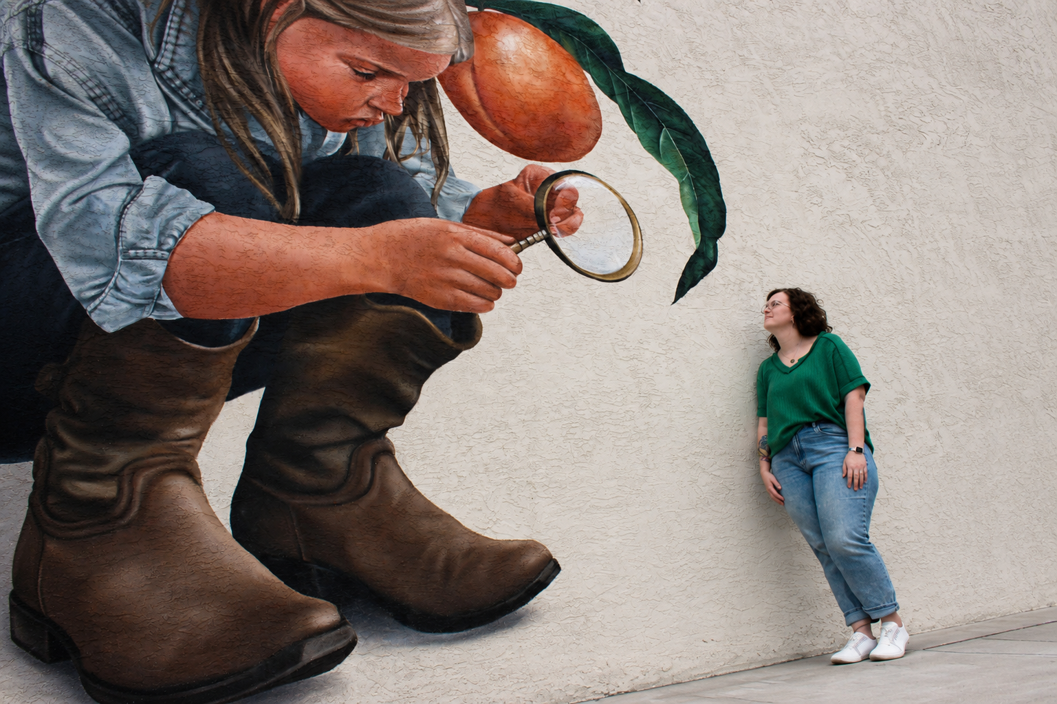 Kalli Stout standing beside a large mural of a child holding a magnifying glass and looking toward the artwork.