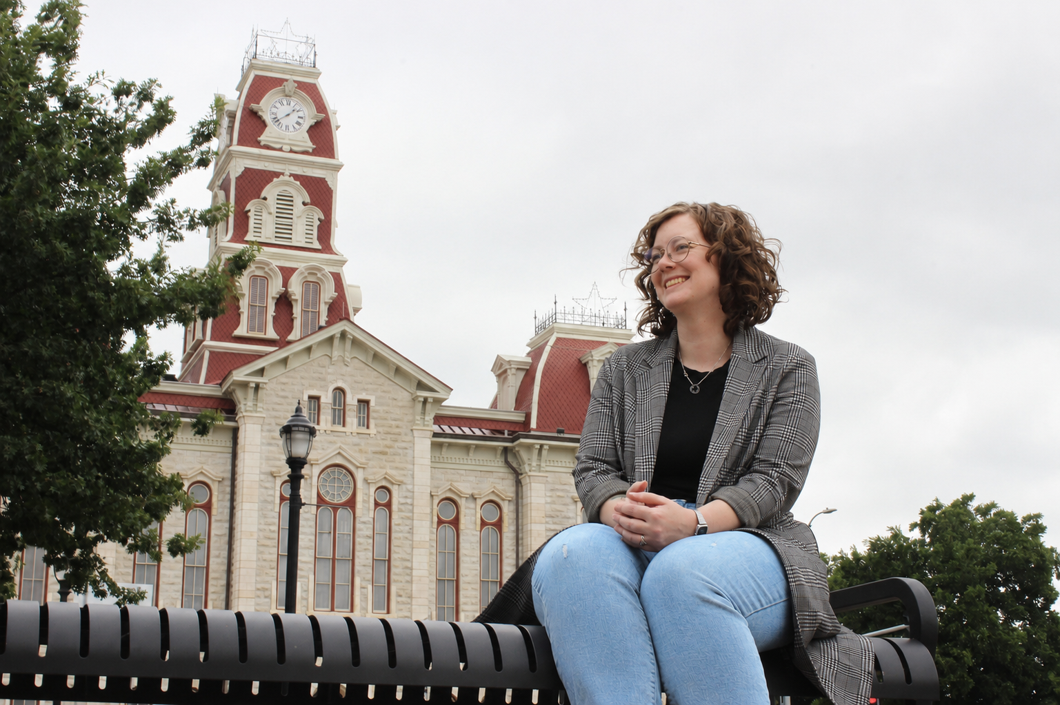 Kalli Stout sitting on a bench in front of the historic Parker County Courthouse in Weatherford, Texas, smiling while looking off into the distance.
