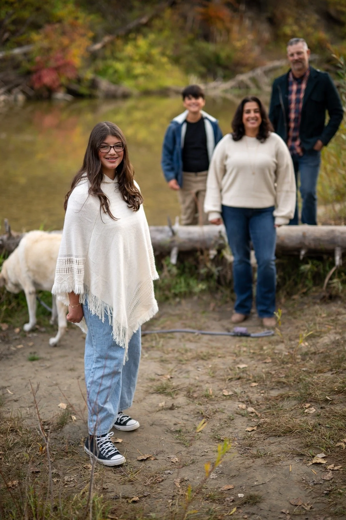 Young woman in sharp focus with her family arranged behind her beside autumn water