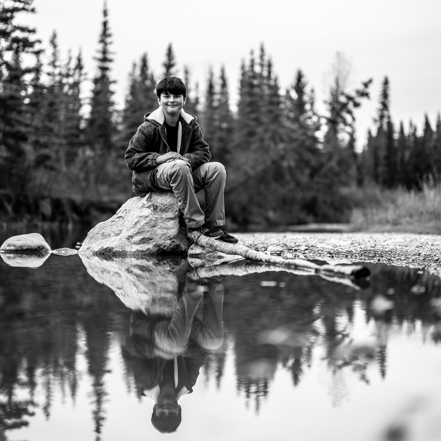 Black-and-white riverside portrait mirrored in calm water