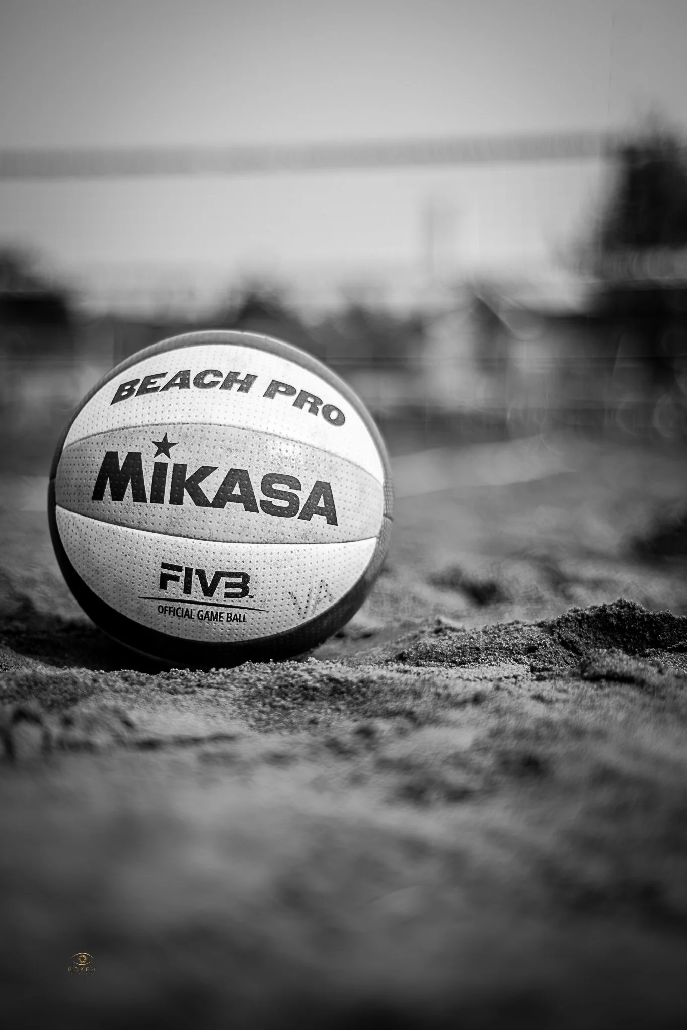 Black-and-white volleyball resting on beach sand with a softly blurred net behind it