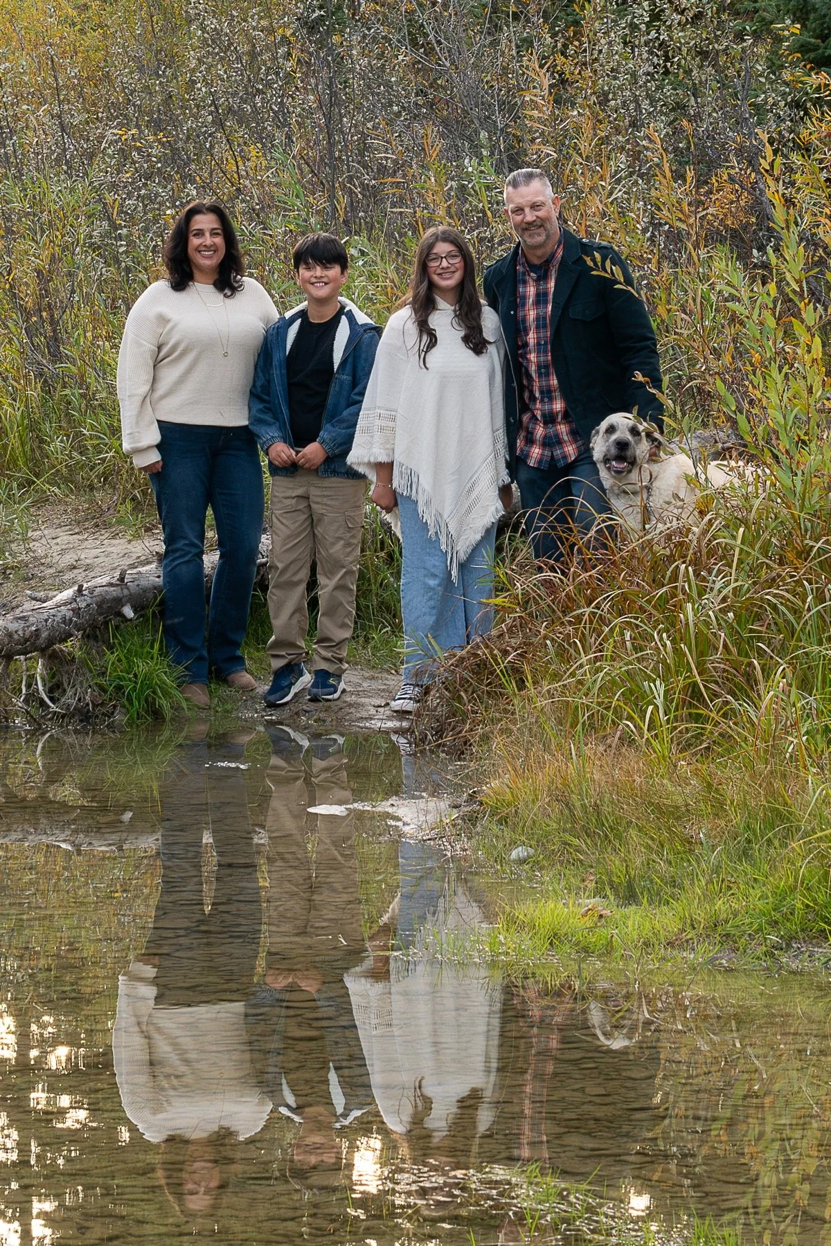 Family and dog standing at the water's edge with their reflections extending below them