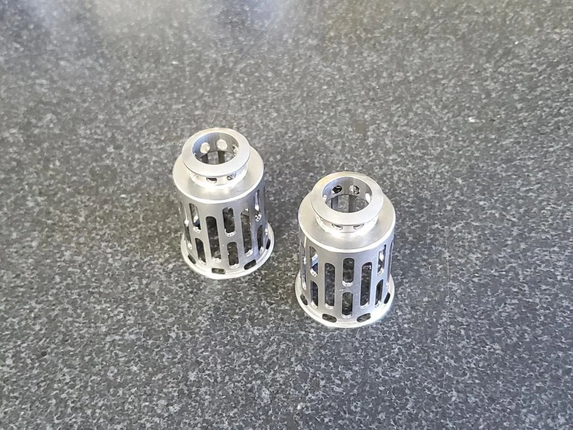 Two metallic cone-shaped objects with cut-out slots, placed on a gray textured surface.