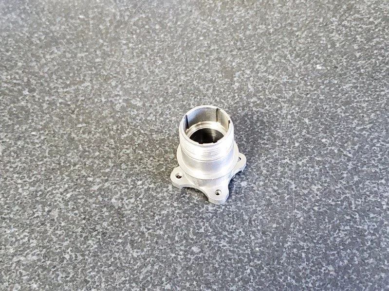 A metal mechanical part, possibly a machined engine component, on a textured gray surface.