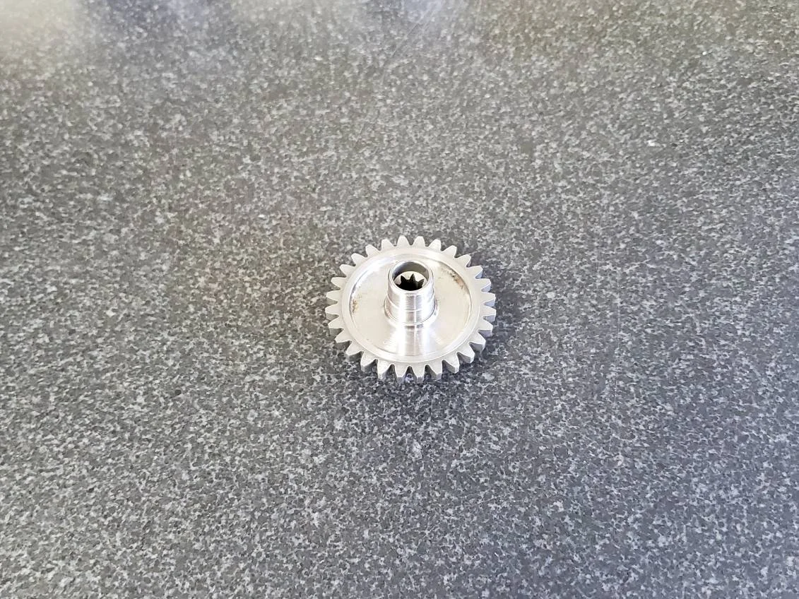 A metallic gear with a central hole featuring internal teeth, placed on a gray textured surface.