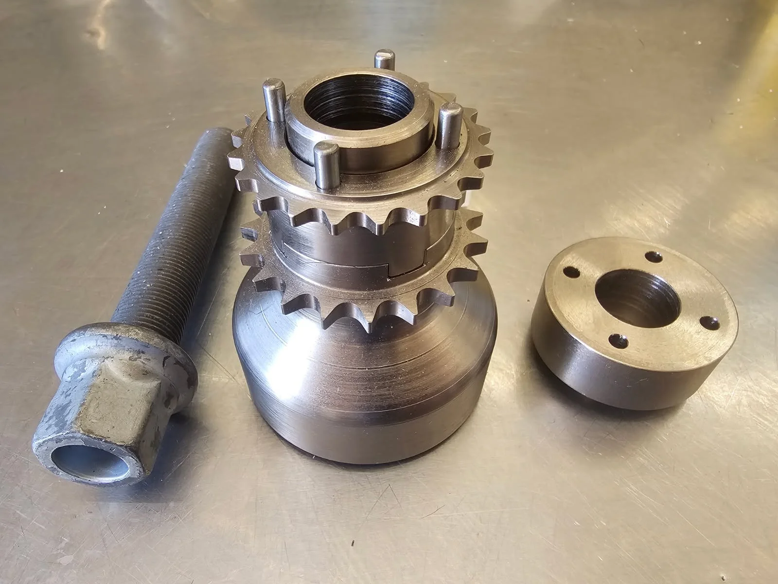 Metal gears stacked with a threaded metal rod and a metal coupling on a metal work surface.