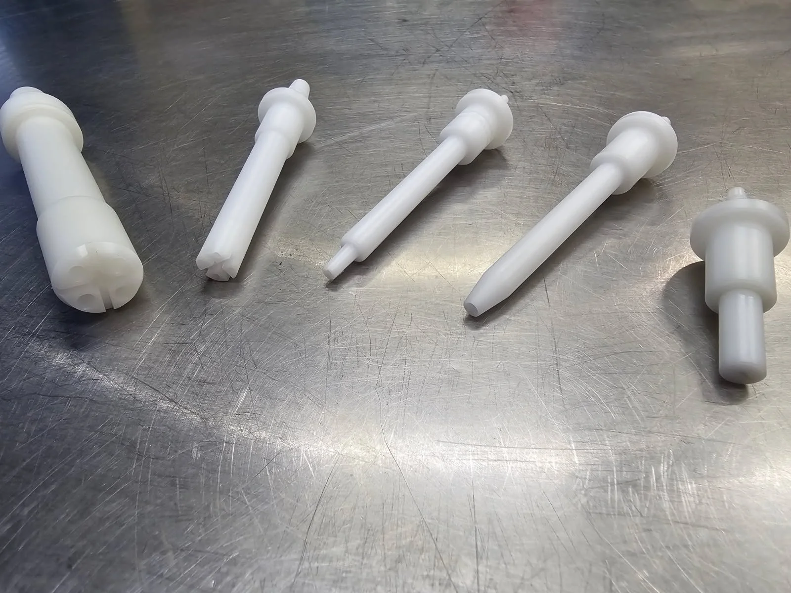Five white plastic orthodontic wax or wax-like devices with different shapes placed on a metal surface.