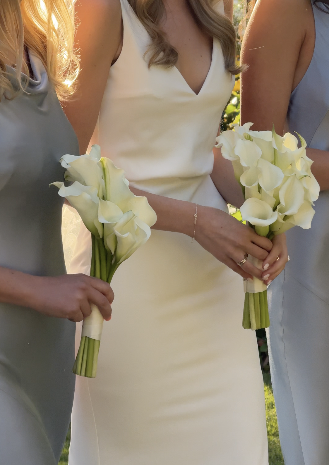 Three women in dresses holding bouquets of white calla lilies at a wedding.