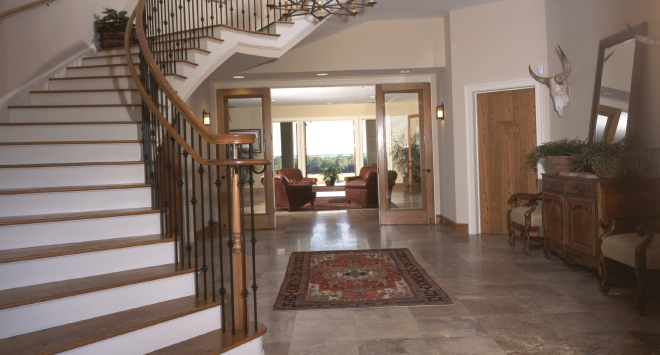 Spacious foyer with a curved staircase, a rug, a wooden sideboard, a mirror, mounted animal skull, and a sitting area visible through glass doors