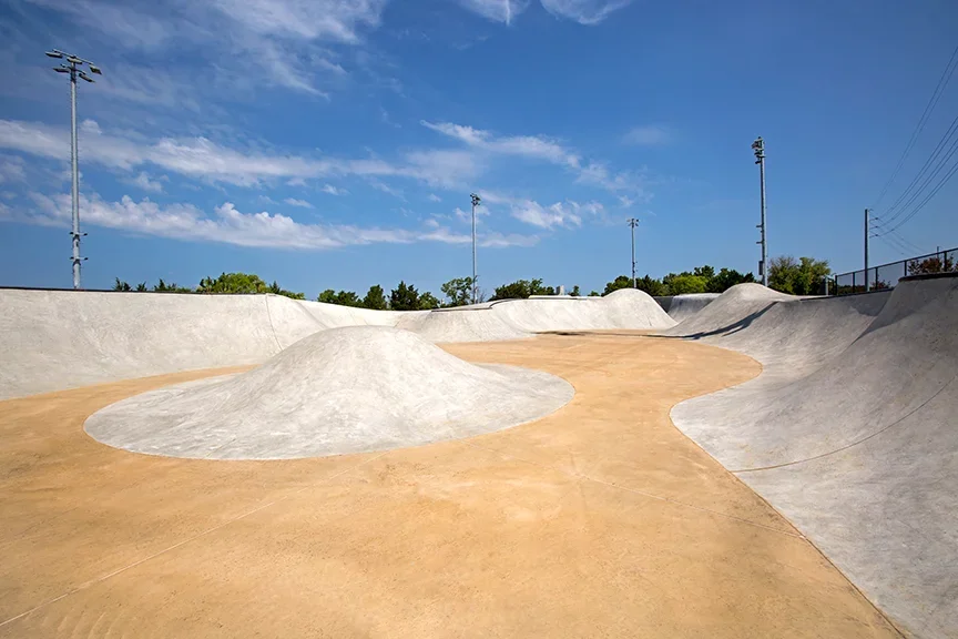 Empty outdoor skate park with concrete ramps and bowls under a blue sky with a few clouds.