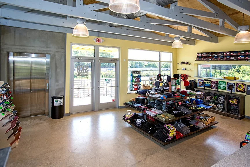 Indoor store with shelves of skate art, hats, and accessories, near glass double doors and windows, with an elevator on the left.