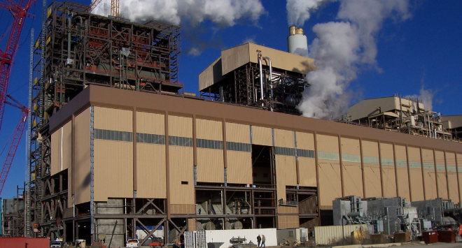 Large industrial factory building with smokestacks emitting smoke under a blue sky with clouds.