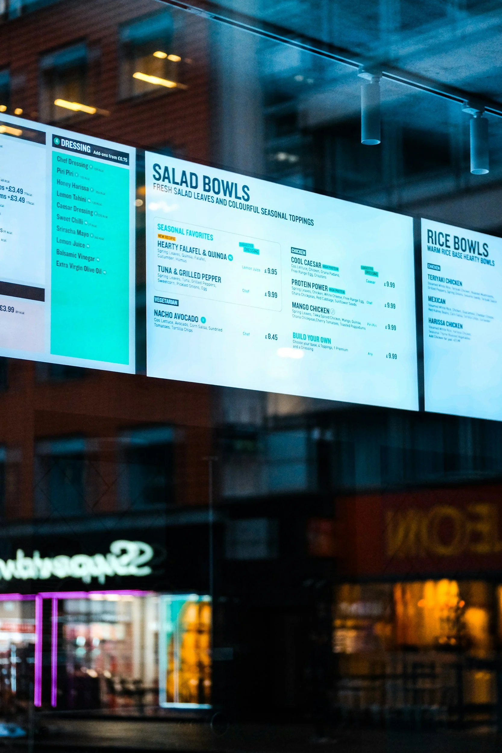 Reflection of brightly lit, professionally installed, storefront digital signage on glass window at night in an urban area.