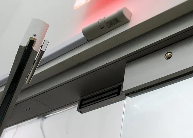 Close-up of a Maglock door lock system mounted onto a glass & metal frame commercial building exterior door.