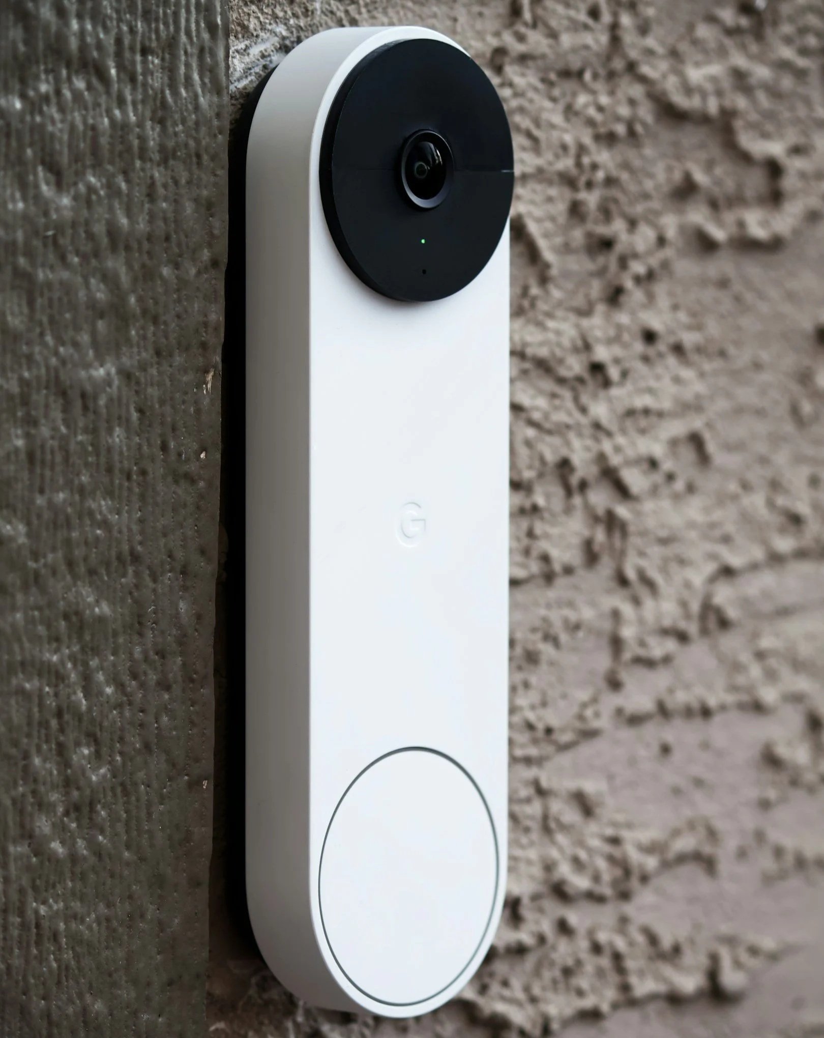 A white smart security video doorbell mounted on a textured brick wall.