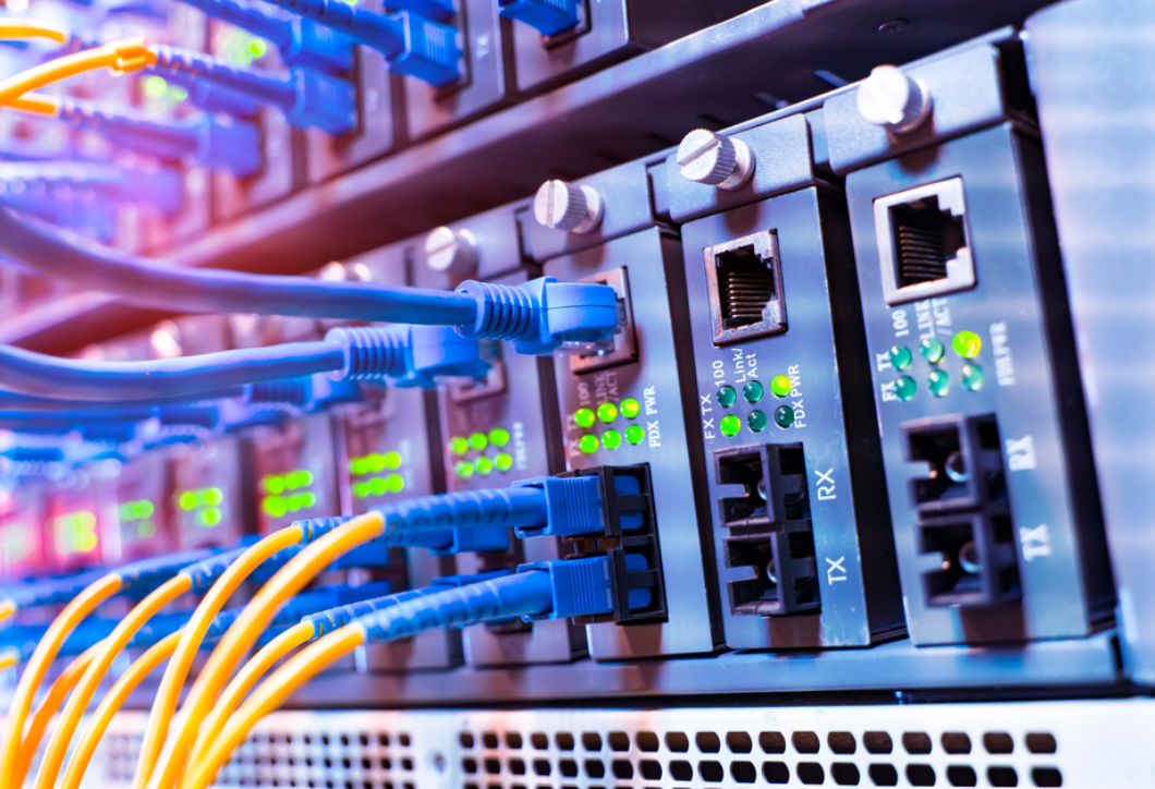 Close-up of network switches with multiple Ethernet cables connected to multiple fiber optic media converters, with pre-terminated fiber optic cables also plugged in, in a data center or server room.