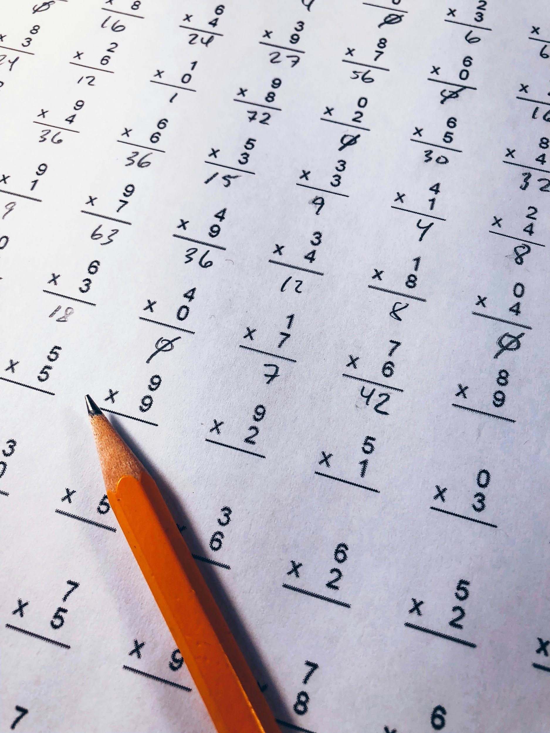 A sheet of paper filled with handwritten math problems, with an orange pencil lying on the paper. Student Support Sheet for Math Tutoring