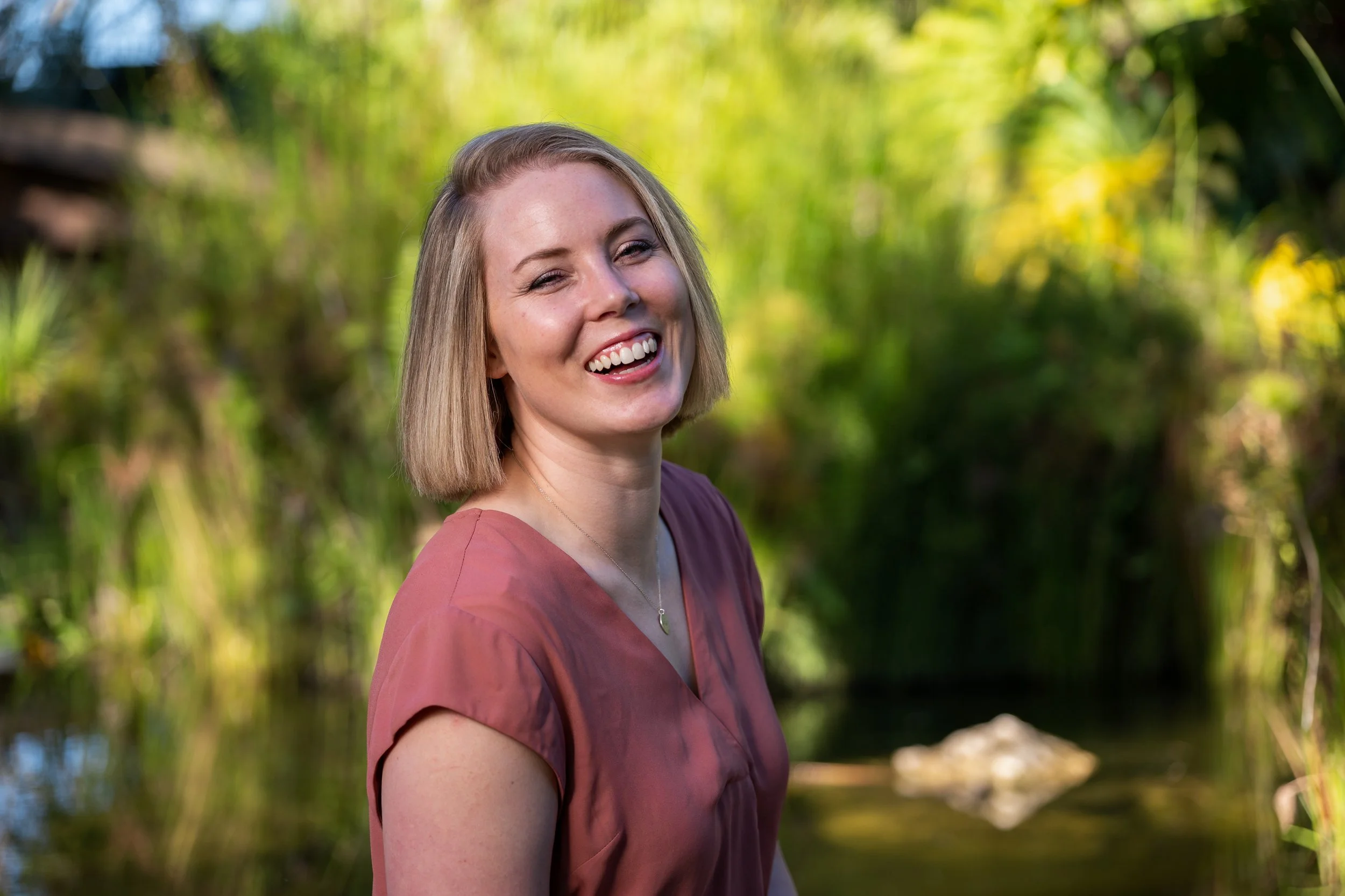 Daneesha, yoga teacher and retreat guide, in a calm outdoor setting with greenery and water in the background
