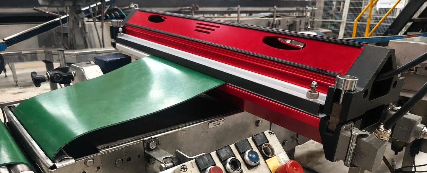 Maquina industrial con banda de transporte verde y una estructura metálica, probablemente utilizada en proceso de fabricación o empaque.