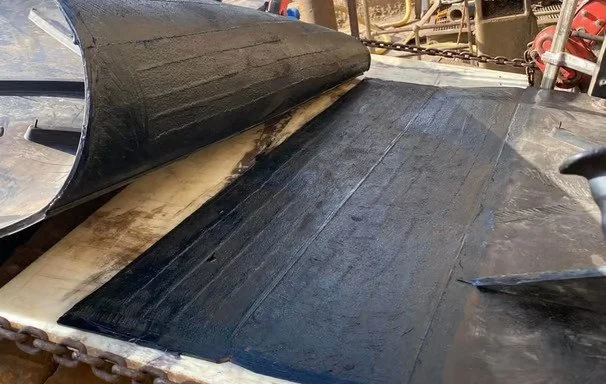 Superficie negra en una estructura metálica con herramientas y maquinaria en el fondo.