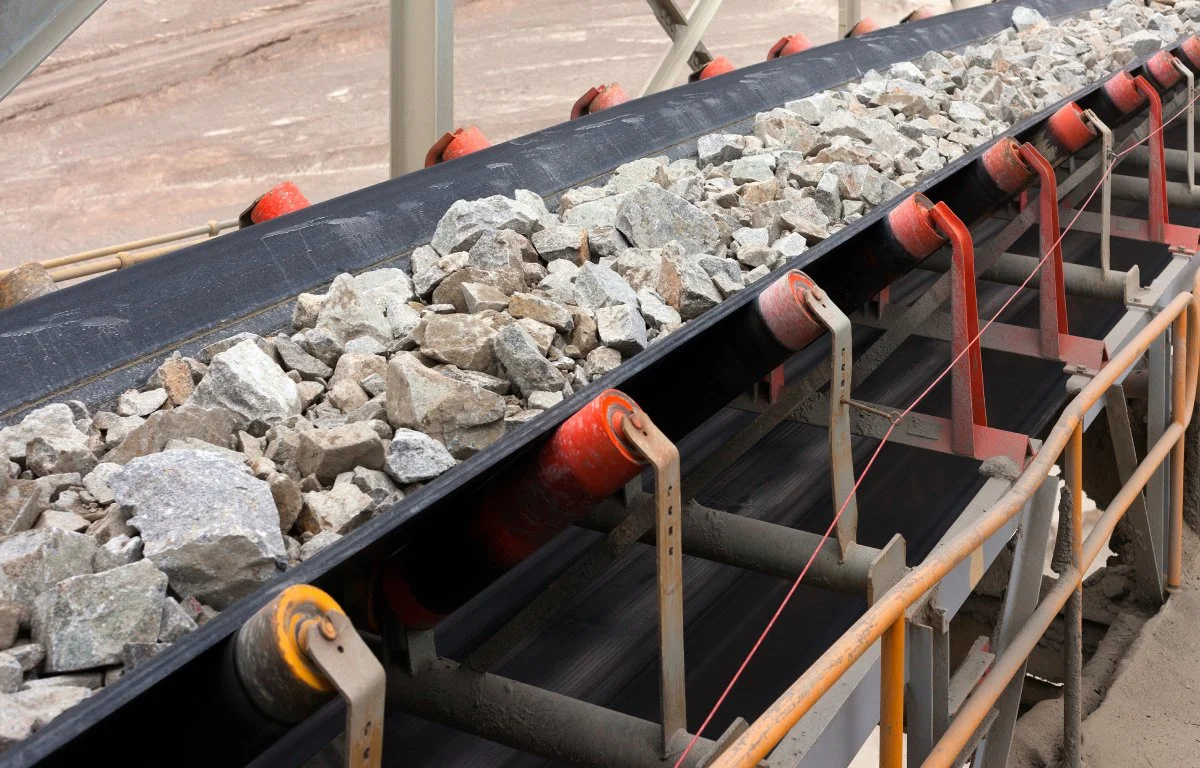 Una cinta transportadora en construcción con rocas en la banda y soportes de metal en los lados.
