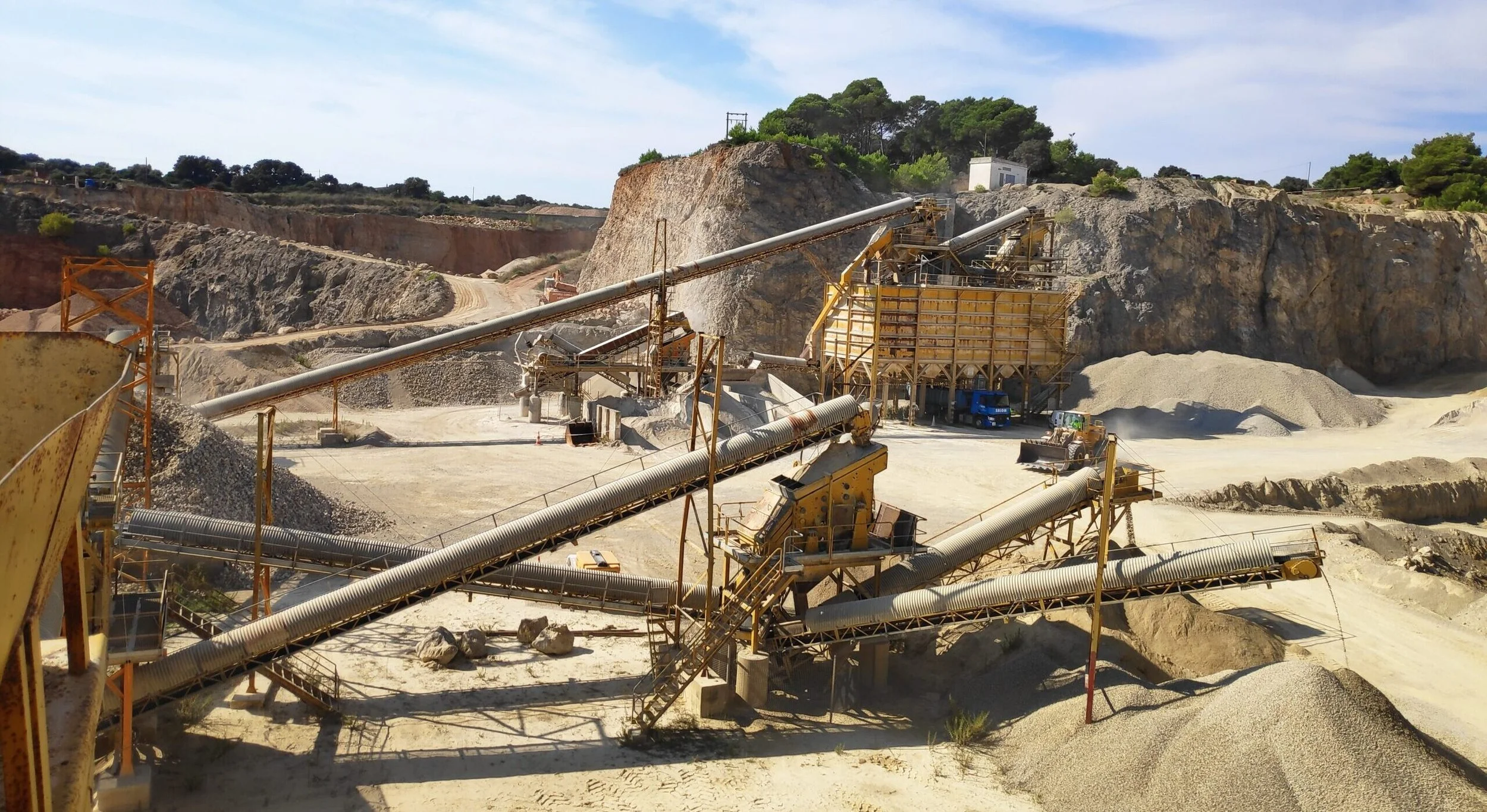 Planta de procesamiento de piedra o mineral en una cantera, con máquinas y cintas transportadoras en un entorno árido y montañoso.