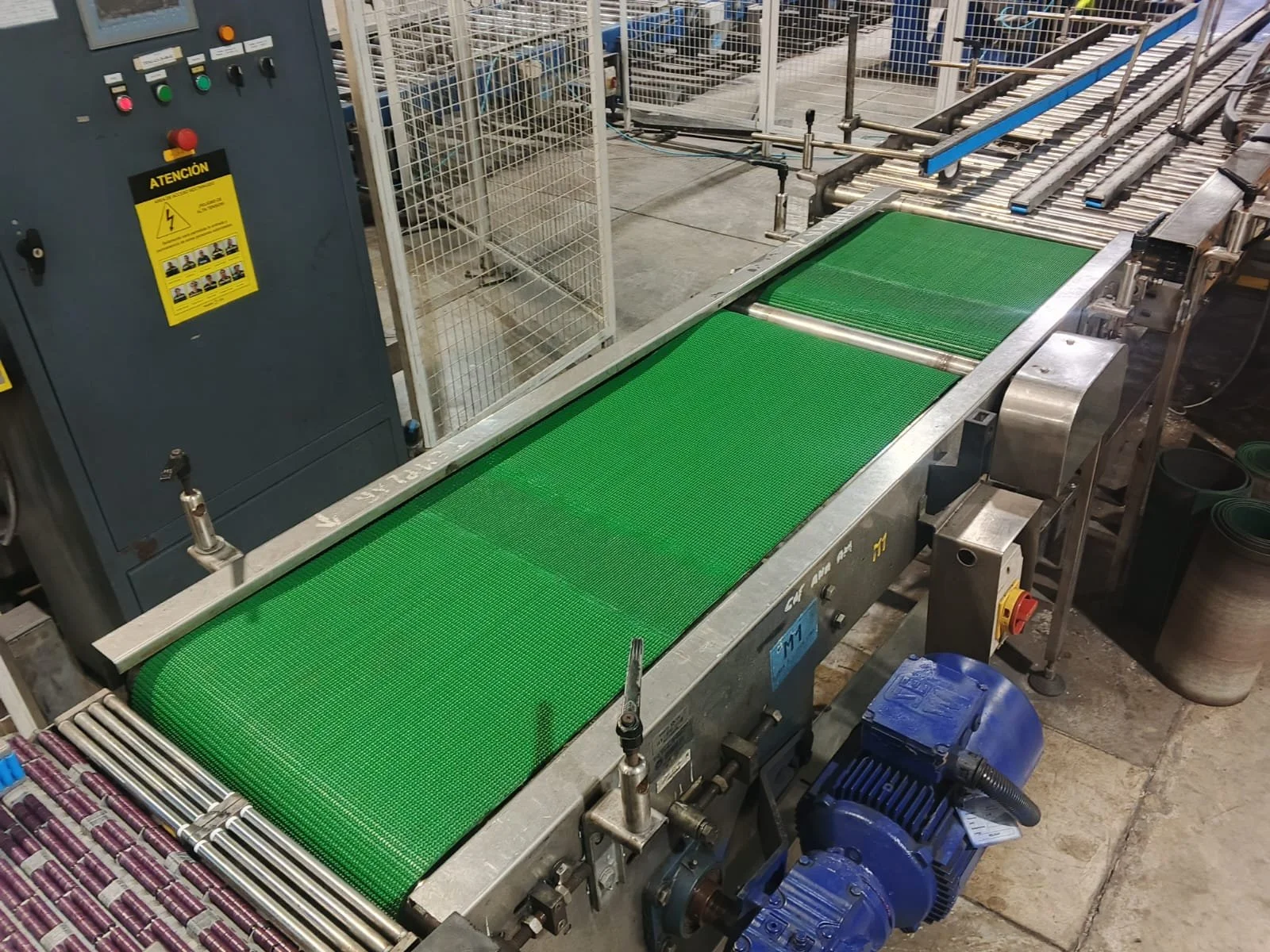 Una línea de producción con cintas transportadoras verdes y maquinaria industrial, ubicada en una fábrica.