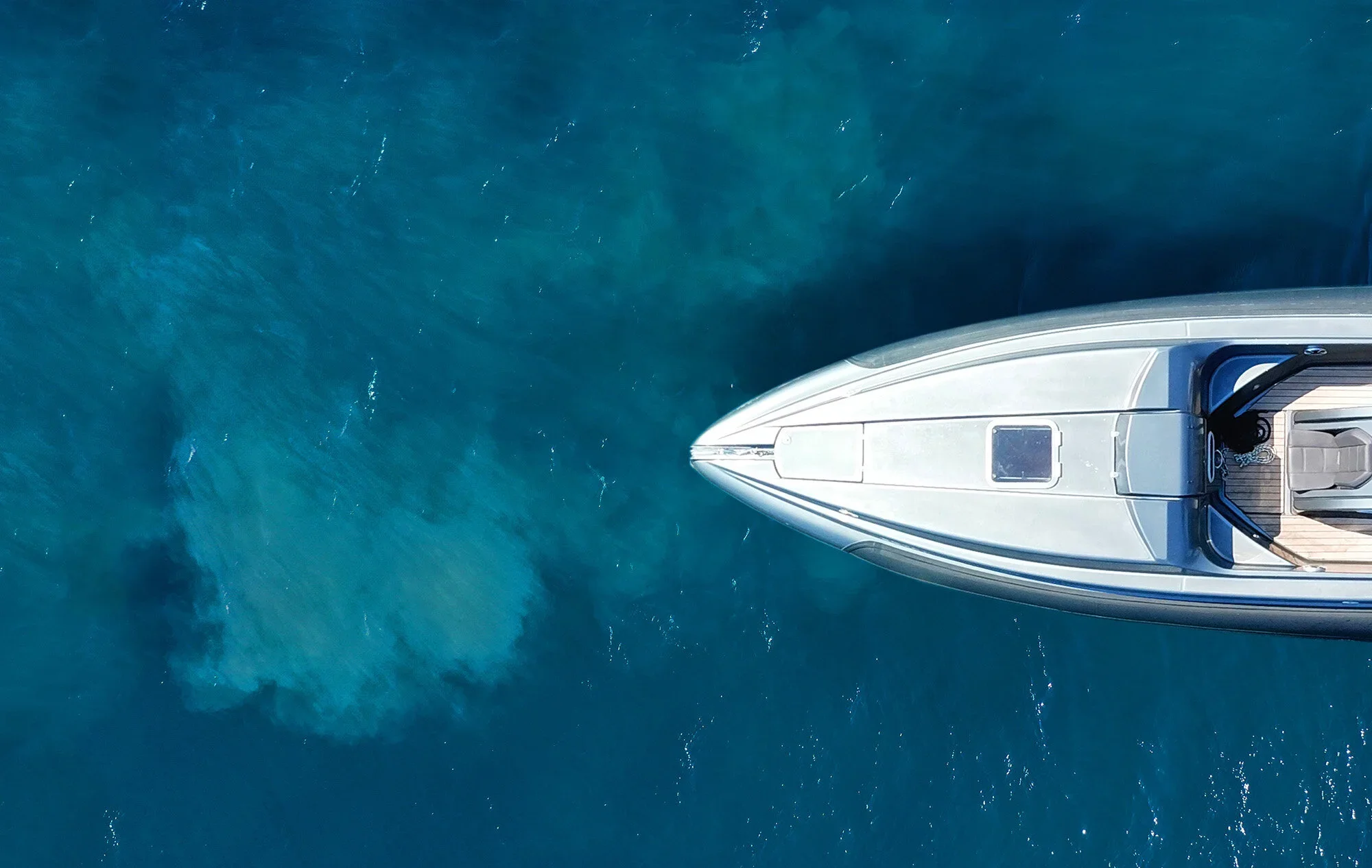 Top-down view of a white yacht with a curved hull, floating on clear blue water.