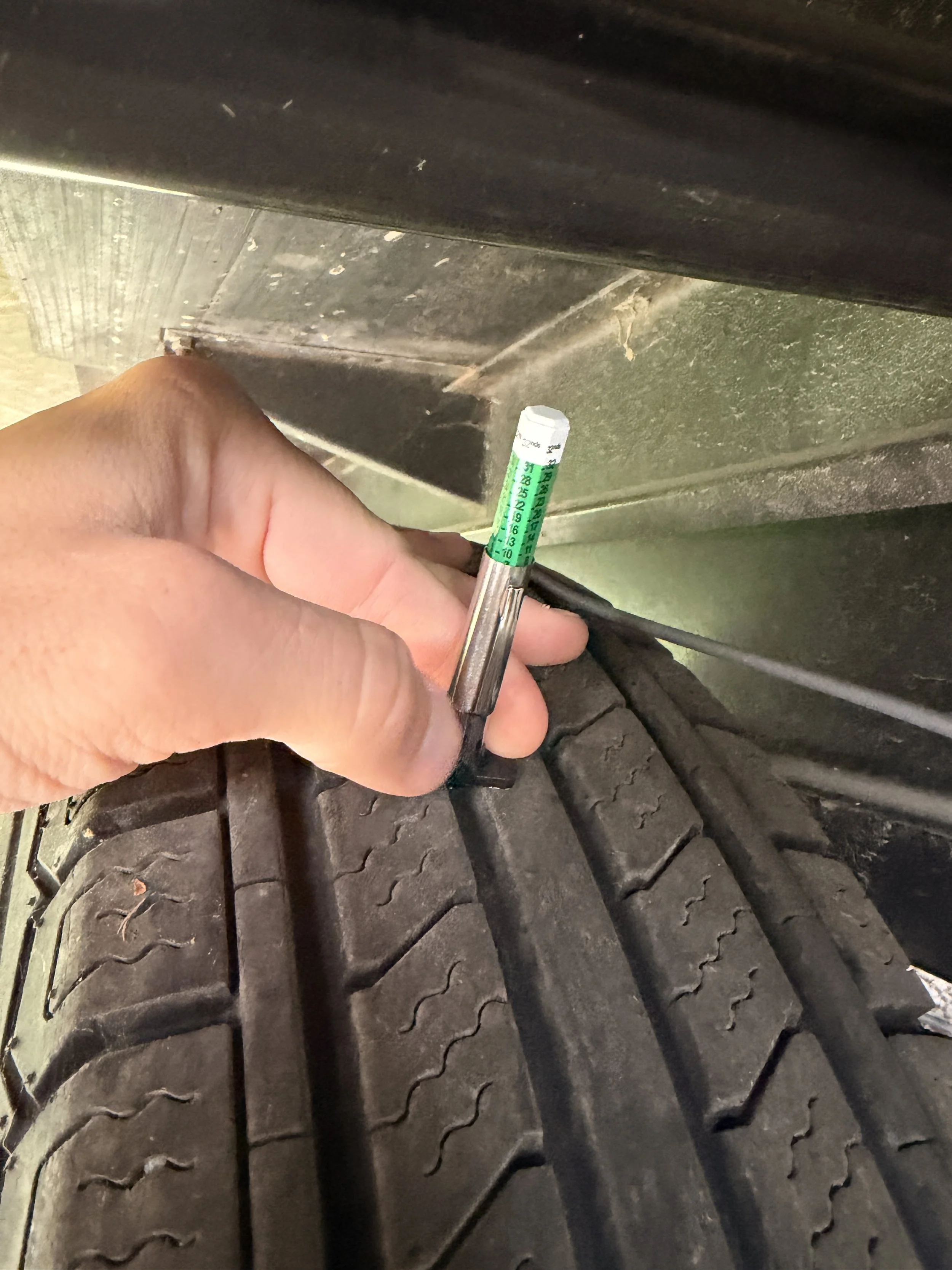 A person's hand holding a tire tread depth gauge measuring the tread depth of a vehicle tire.