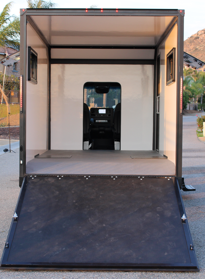 Empty mobile office or tiny home on wheels with an interior view showing a driver's seat and a dashboard through the open rear ramp.