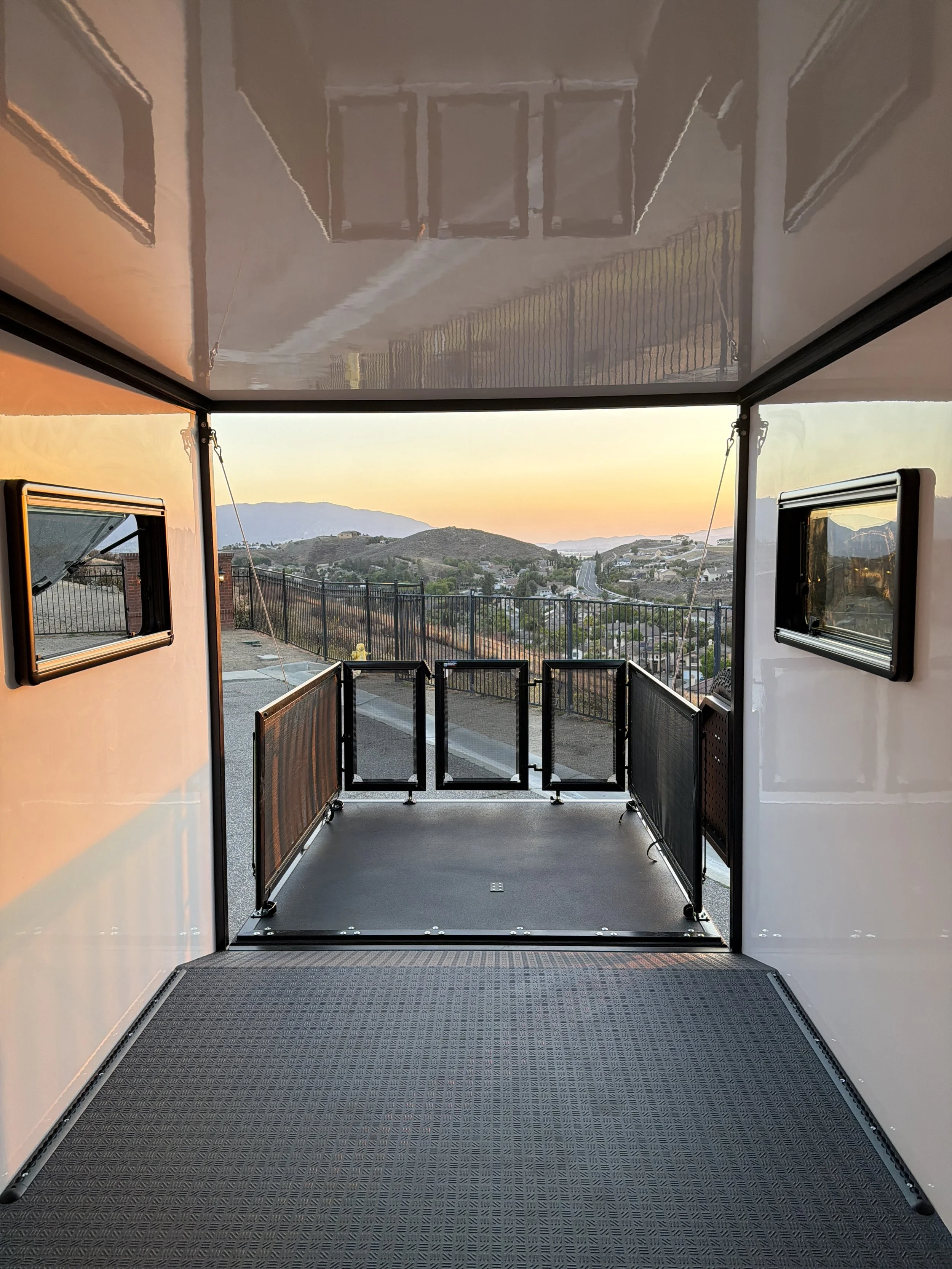 View from inside an enclosed transportation vehicle looking out toward a scenic landscape with hills and homes at sunset.