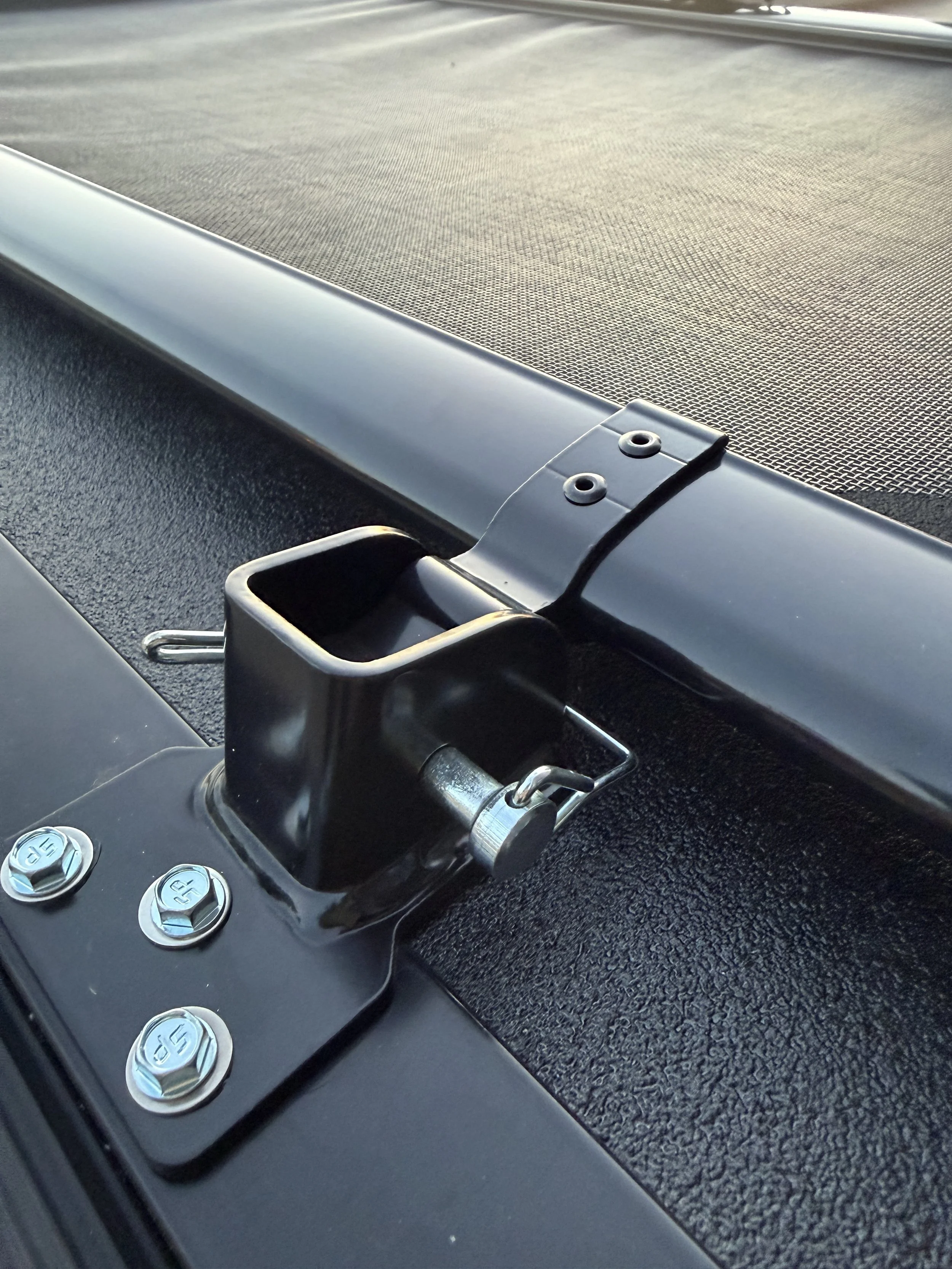 Close-up of a metal mount with a hinge on a black textured surface, part of a vehicle, with screws and buttons labeled 'A' and 'B' visible nearby.