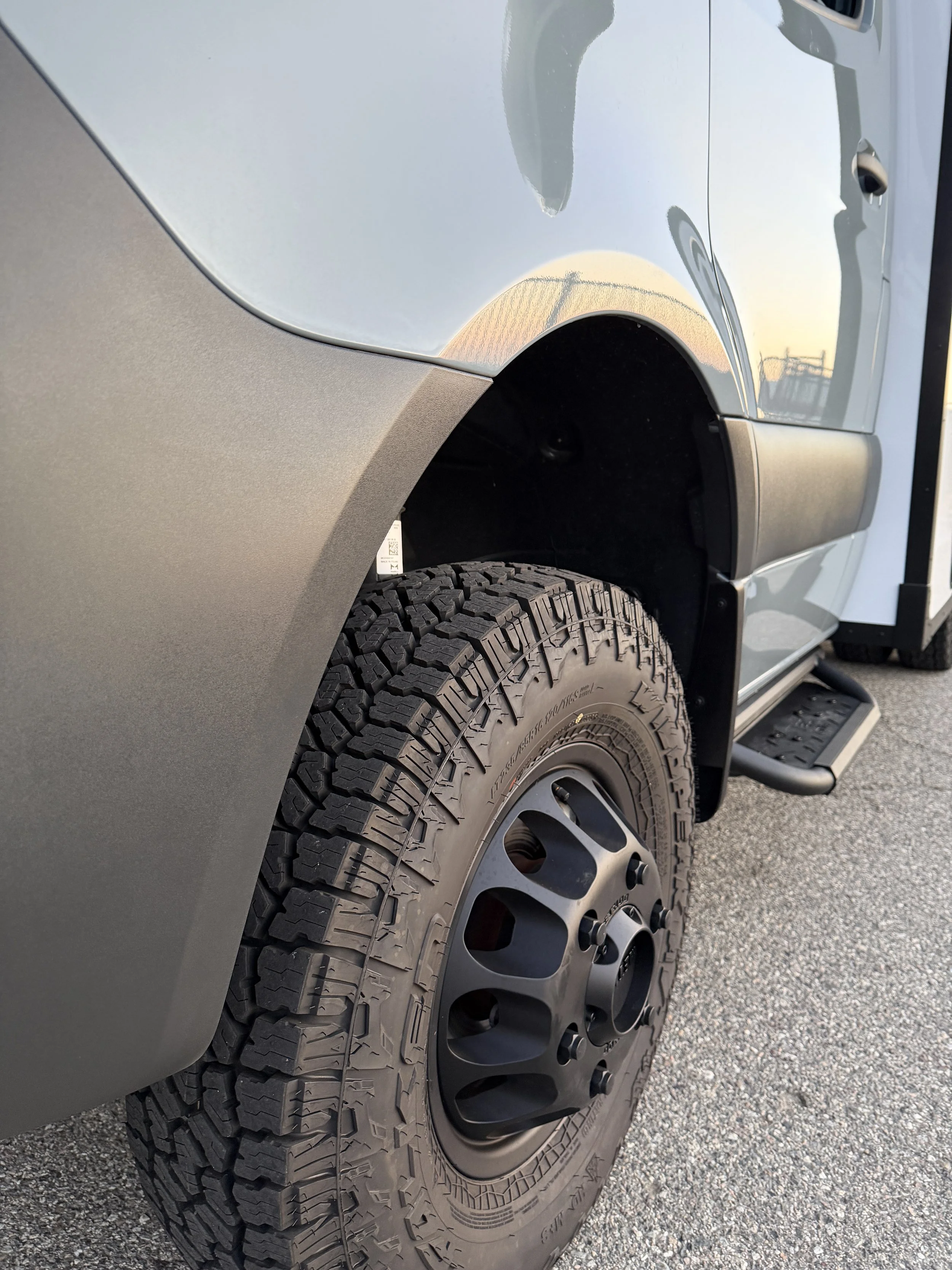Close-up of the front tire and wheel of a light gray pickup truck parked on asphalt.